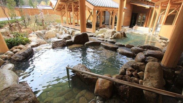 Een traditionele Japanse onsen met een houten badhuis, een vijver met rotsen en een pad van stenen.