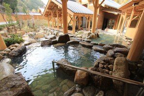 Ein traditionelles japanisches Onsen mit Holzbädern, einem steinigen Teich und einem Kiesweg.