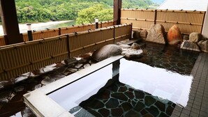 Een traditioneel Japans onsen met uitzicht op een bebost gebergte en een rivier.