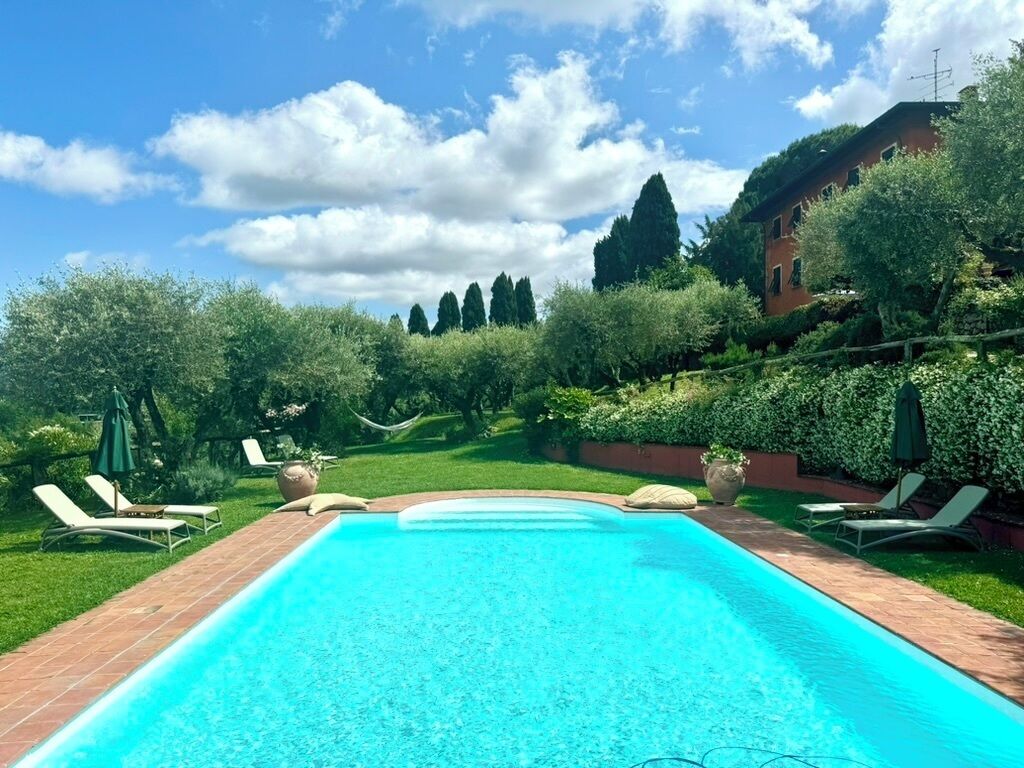 Ein rechteckiger Pool mit Fliesenrand, umgeben von einer Ziegelterrasse. Am Poolufer stehen Liegestühle und Sonnenschirme.
