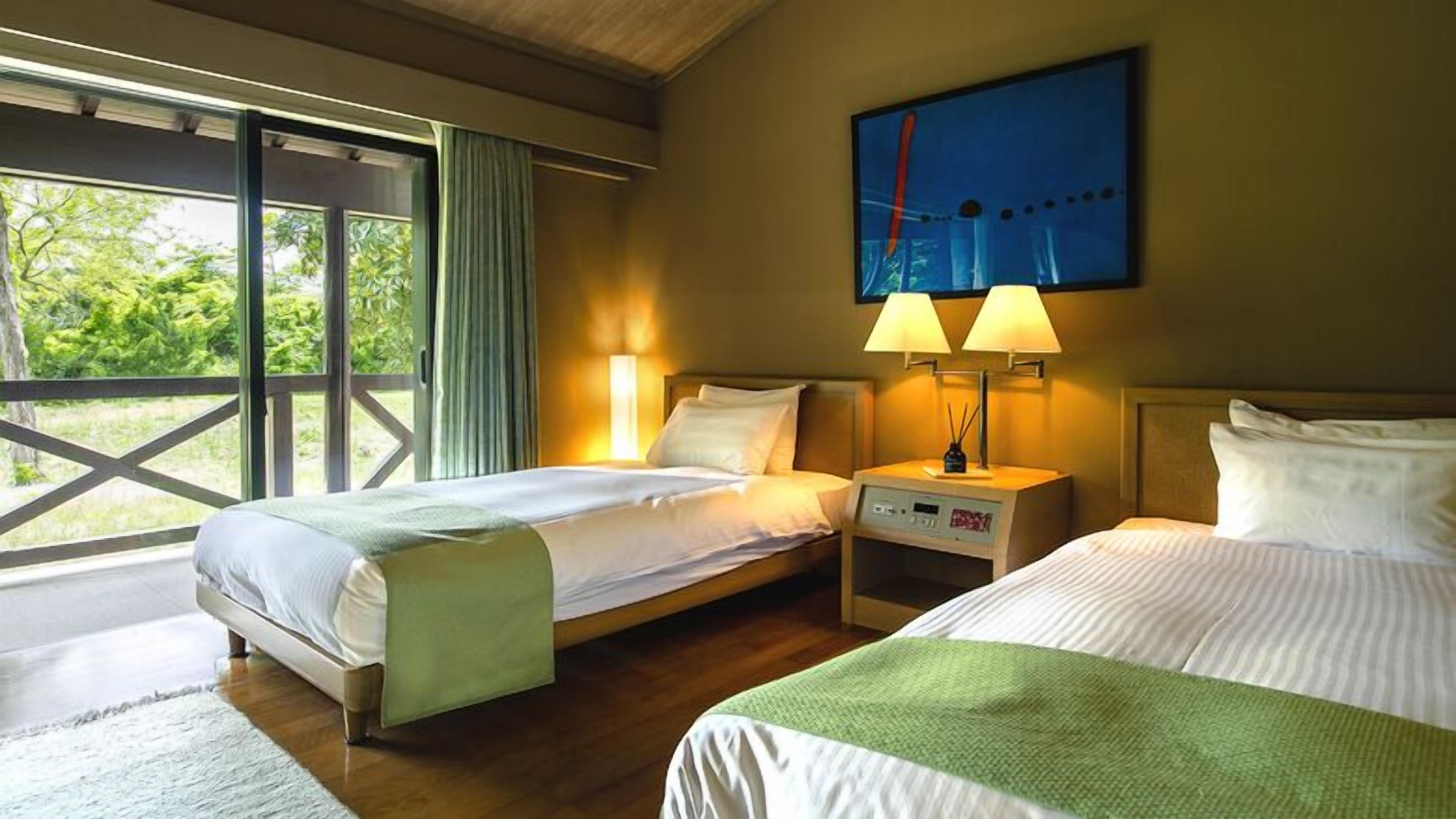A hotel room with two beds, a large window, and a painting on the wall.