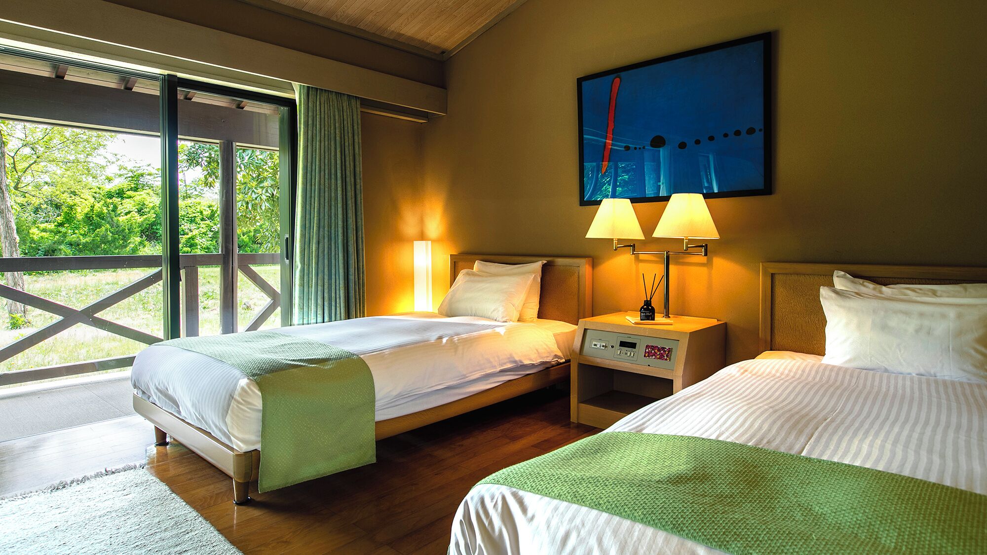 A hotel room with two beds, a large window, a painting, and a nightstand with a lamp.