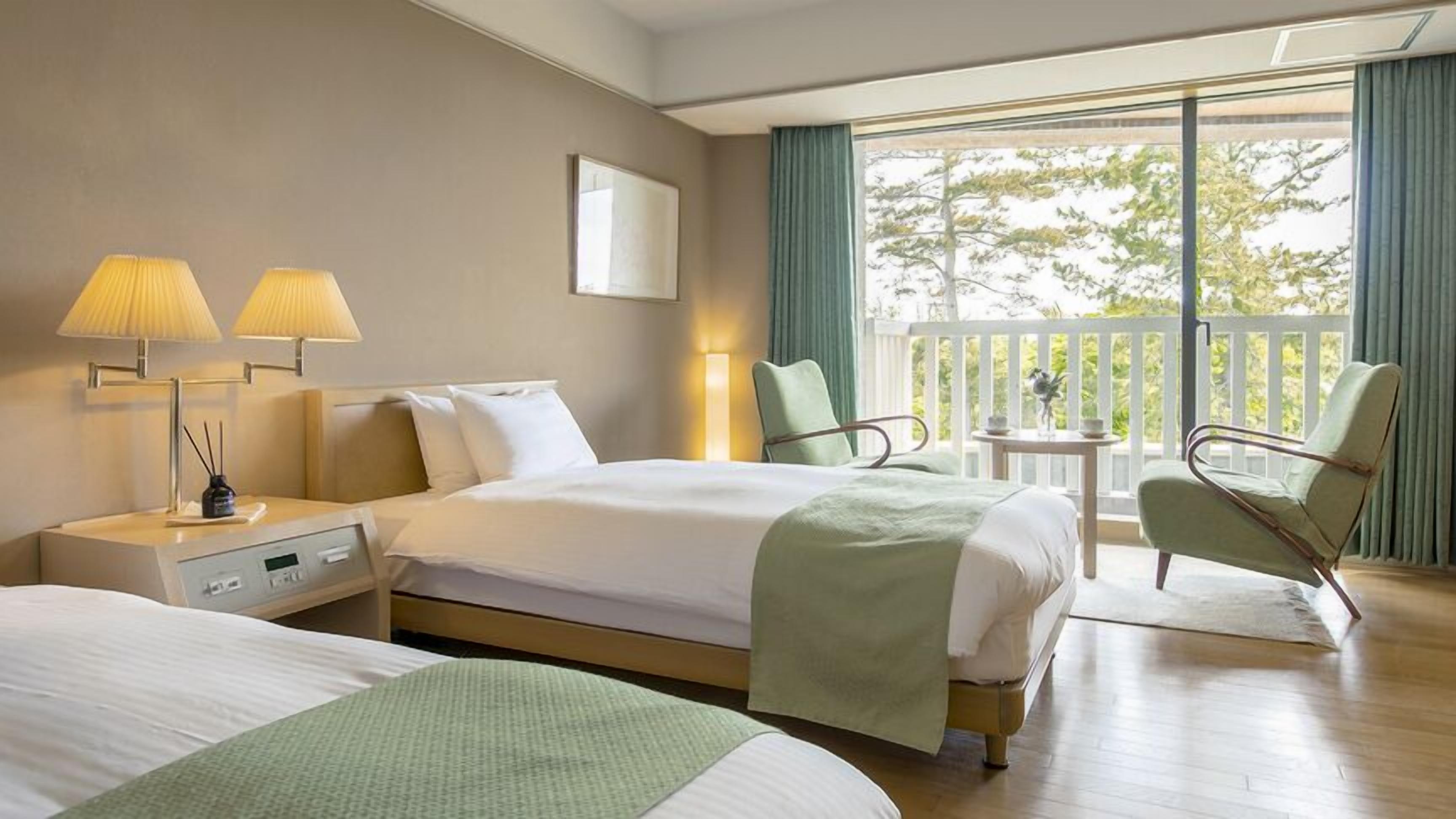 Habitació d'hotel amb dos llits, una taula de nit, una làmpada, una cadira i un balcó amb vistes.