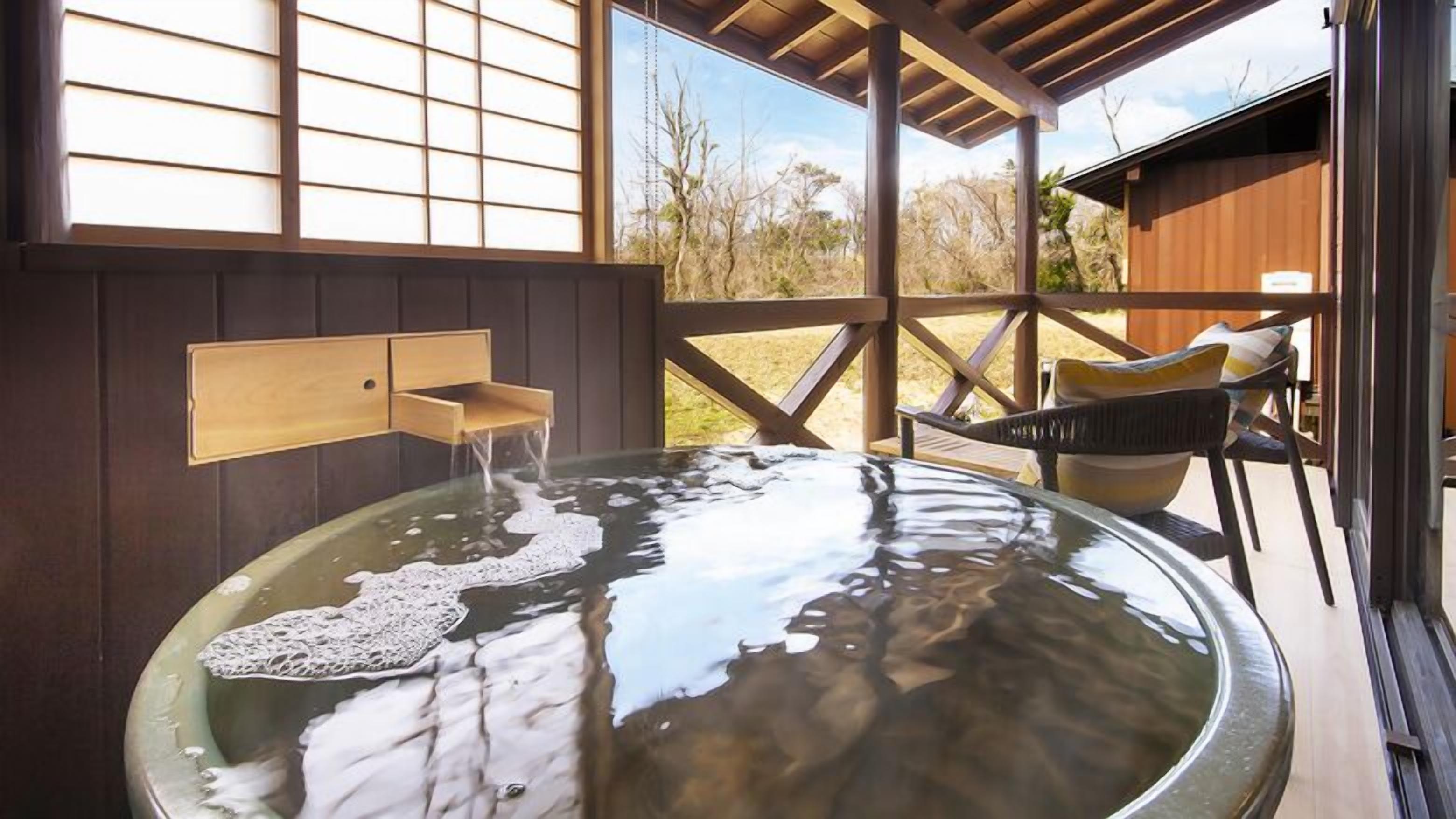 A hot tub with a wooden wall-mounted faucet, a wooden deck, and a view of the outdoors.
