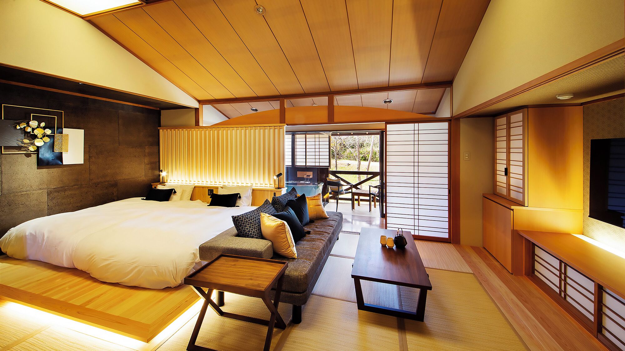 A traditional Japanese-style bedroom with a large bed, a sofa, a small table, and a TV.