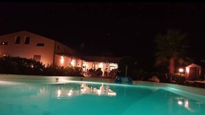 Uma piscina à noite, com um edifício ao fundo.