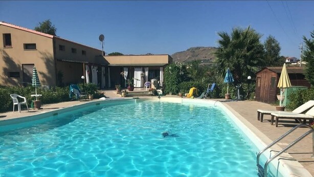 Piscina com águas azuis cristalinas, rodeada por espreguiçadeiras e guarda-sóis, com um edifício ao fundo.
