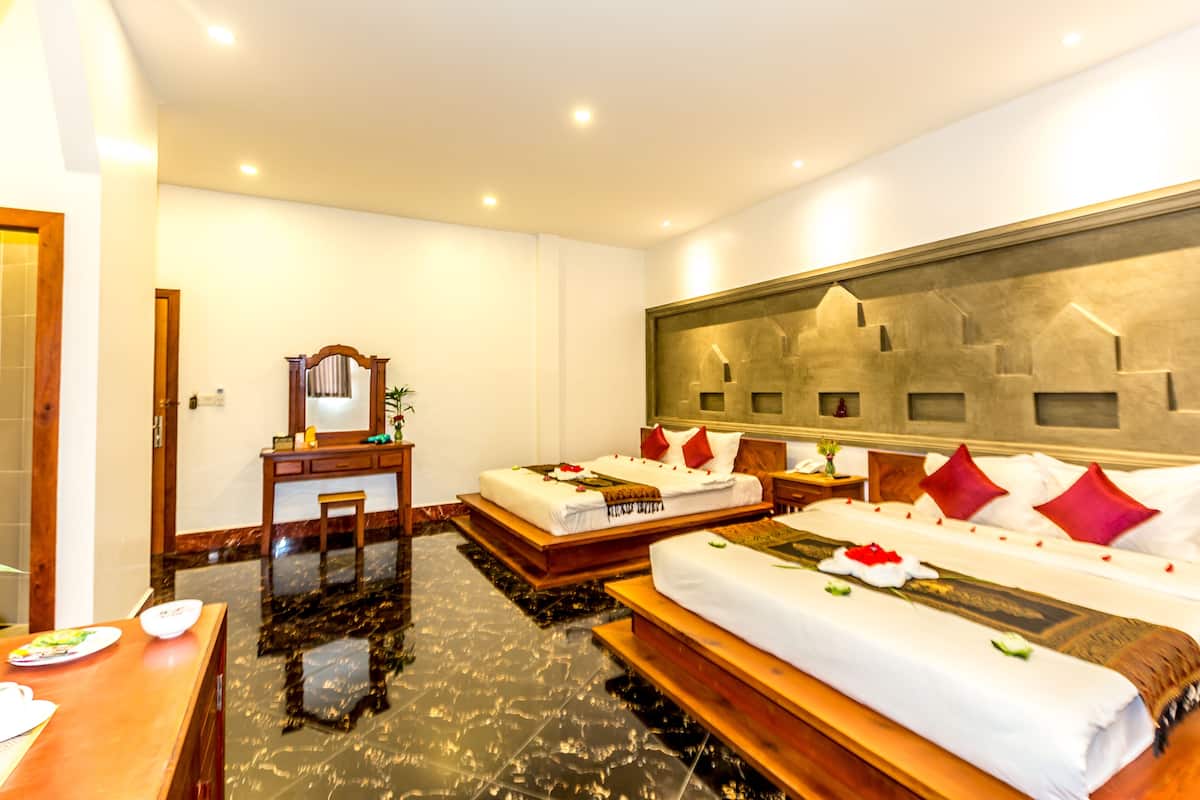 Habitación de hotel con dos camas, un escritorio, una silla y un espejo grande.