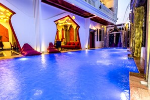 A spacious indoor pool area with a blue floor, red seating, and a balcony overlooking the pool.