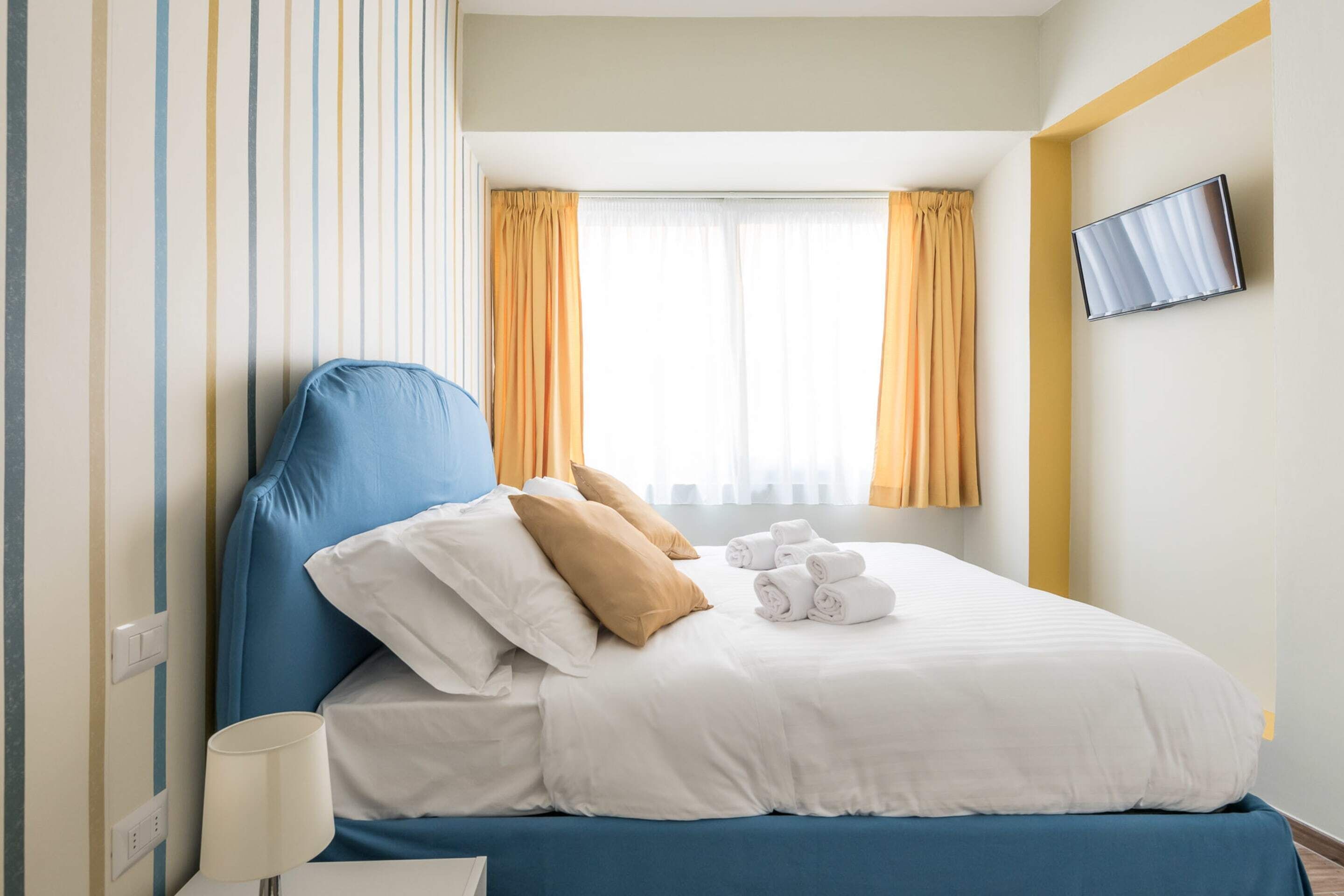 Une chambre d’hôtel avec un lit, des oreillers, une télévision et une fenêtre avec des rideaux.