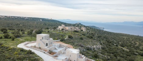 Um complexo de edifícios à beira-mar, com várias estruturas, rodeado por vegetação nativa e vista para o oceano.