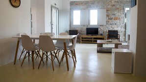 Ein modernes Wohnzimmer mit Steinwand, einem Essbereich mit weißem Tisch und Stühlen sowie einer kleinen weißen Kommode.