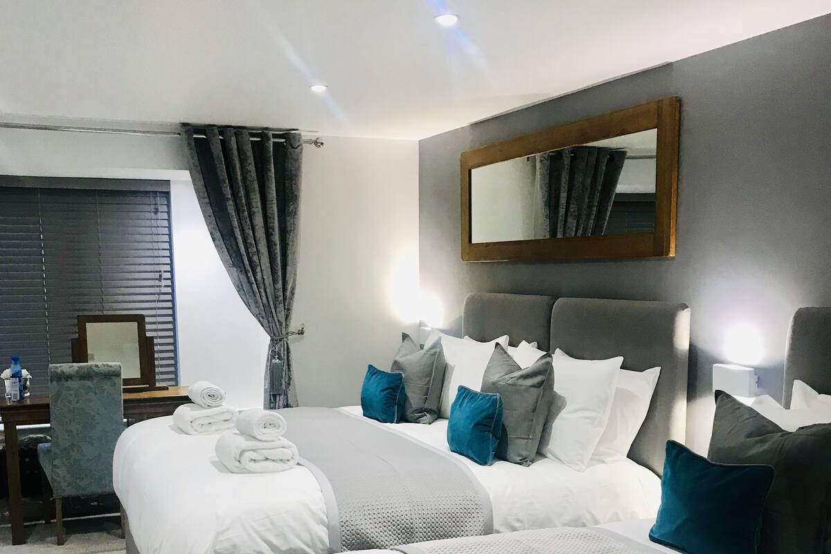 A modern hotel room with two large beds, a desk, and a chair.