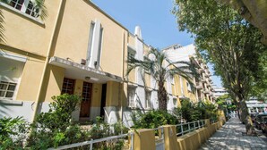 Un bâtiment jaune avec des balcons, un palmier et un trottoir.