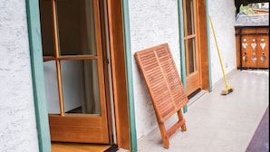 A building with two large wooden-framed windows with green trim, a wooden bench, and a broom leaning against the wall.