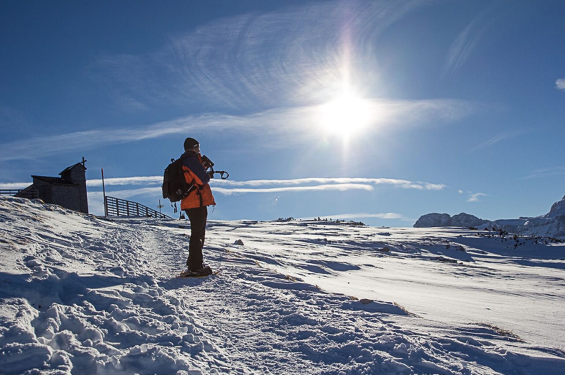 A person standing on a snowy slope with a clear sky and sun.