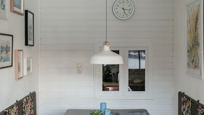 A dining area with a wooden table, blue chairs, and a bench. There is a clock on the wall and framed pictures on the wall.