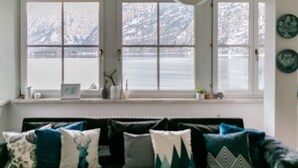 A cozy living room with a dark-colored sofa adorned with patterned cushions, a window with a view of a snowy landscape, and a white ceiling fan.
