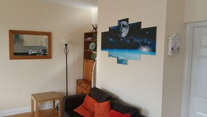 Ein Wohnzimmer mit einer schwarzen Couch, einem kleinen Holztisch, einer Stehlampe, einem Bücherregal und einem Wandbild mit Mond und Sternen.