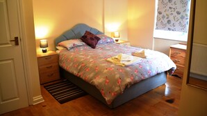 Ein Schlafzimmer mit Bett, Nachttischen, einem Fenster mit floralem Vorhang und einem Heizkörper.