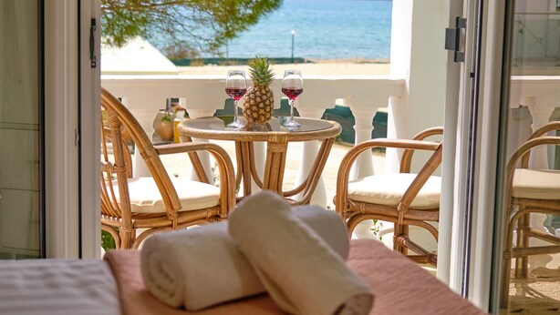 Ein Balkon mit Korbstühlen, einem kleinen runden Tisch, zwei Weingläsern und einer Ananas, mit Blick auf das Meer.