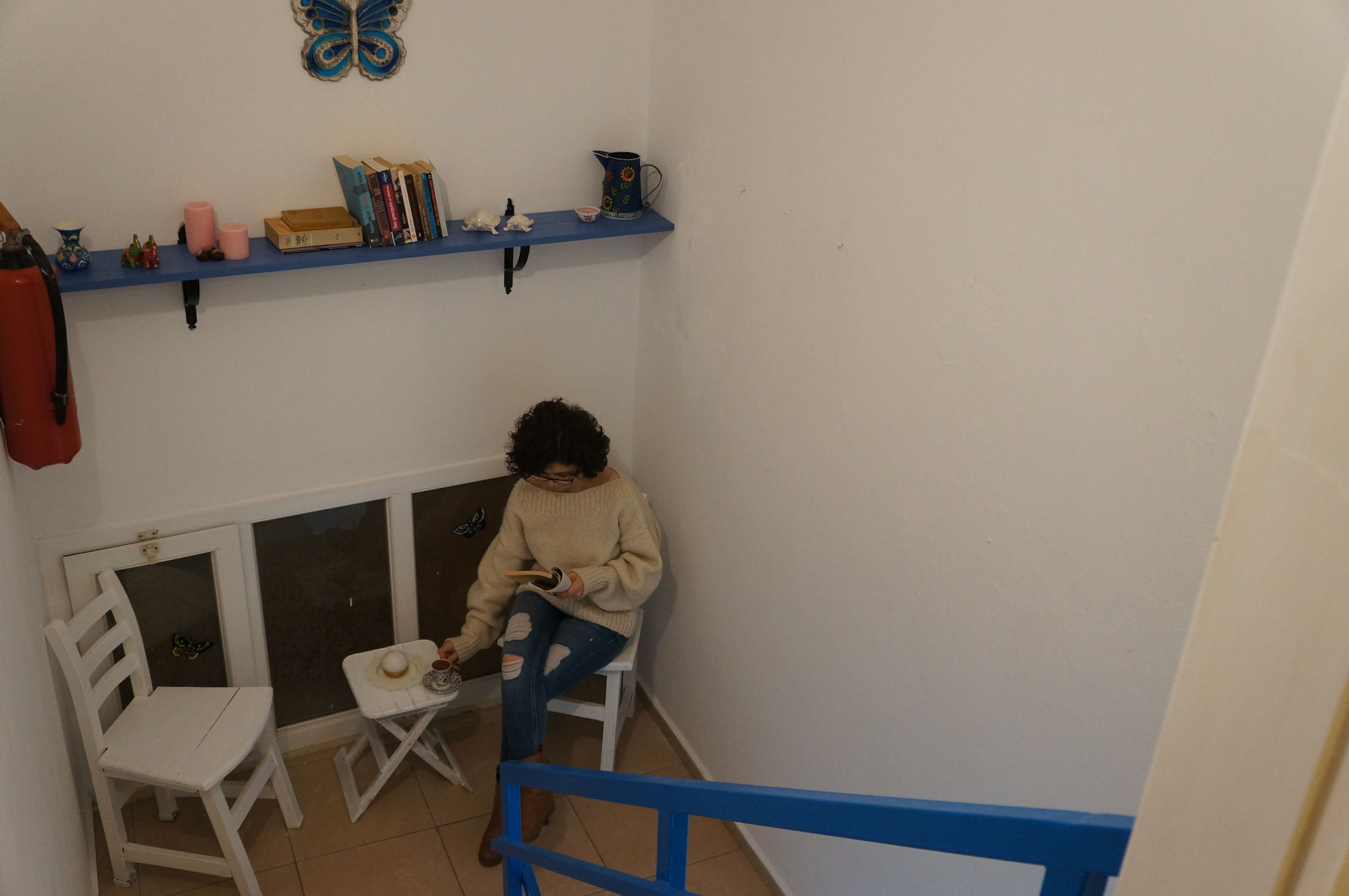 A small room with a white chair, a table, and a blue shelf with books and decorative items.