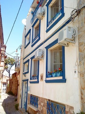 A two-story building with blue-framed windows and balconies, stone walls, and a narrow street.