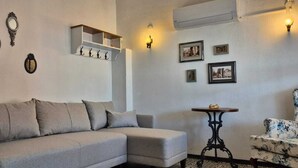 A living room with a sofa, a small table, a chair, wall-mounted decor, and an air conditioning unit. - Kelebek Ayvalık (Ayvalik)