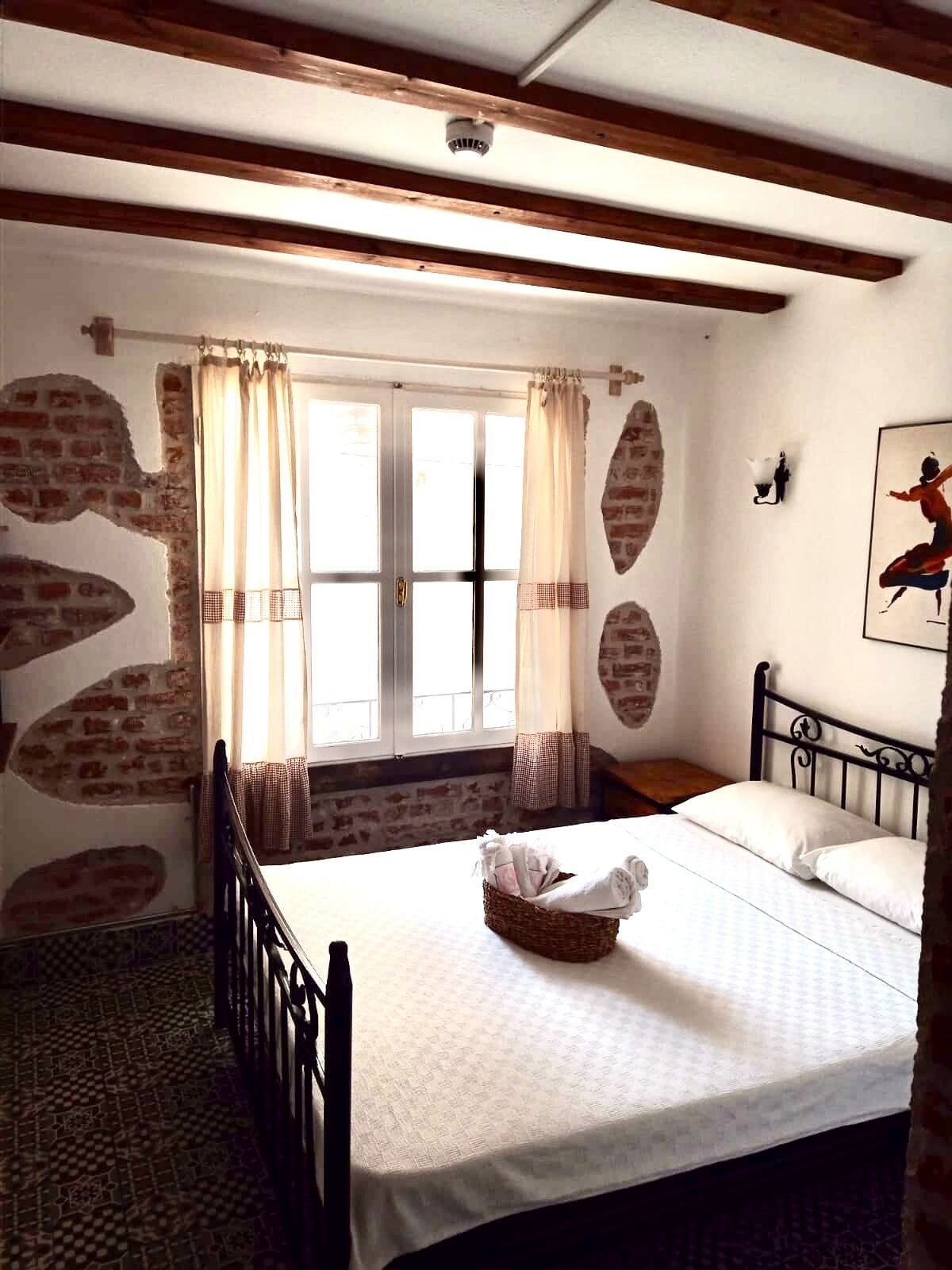 Une chambre à coucher avec un lit, une fenêtre avec des rideaux, un mur avec un motif en briques et un tableau accroché au mur.