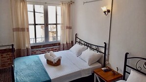 A bedroom with a bed, a bedside table, a nightstand, a window with curtains, and a wall-mounted lamp. - Kelebek Ayvalık (Ayvalik)