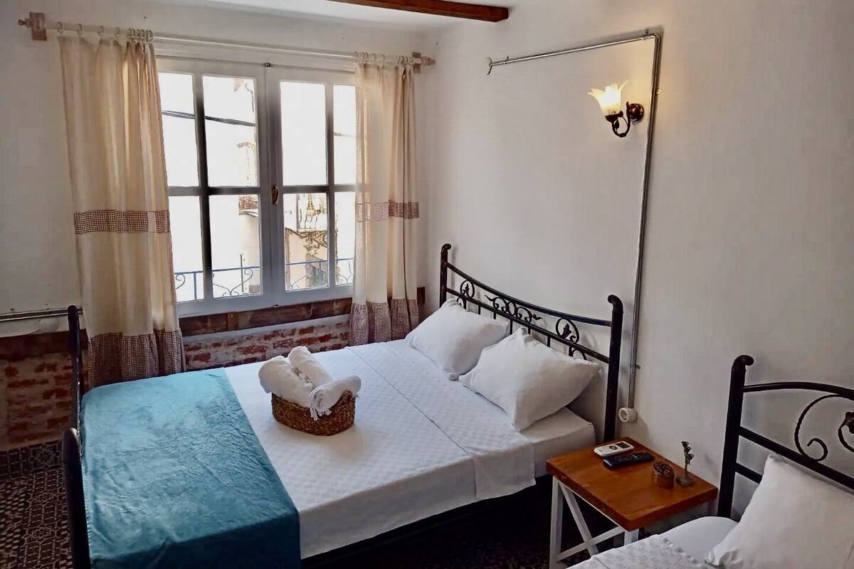 Un dormitorio con cama, mesita de noche, cortinas en la ventana y una lámpara de pared.