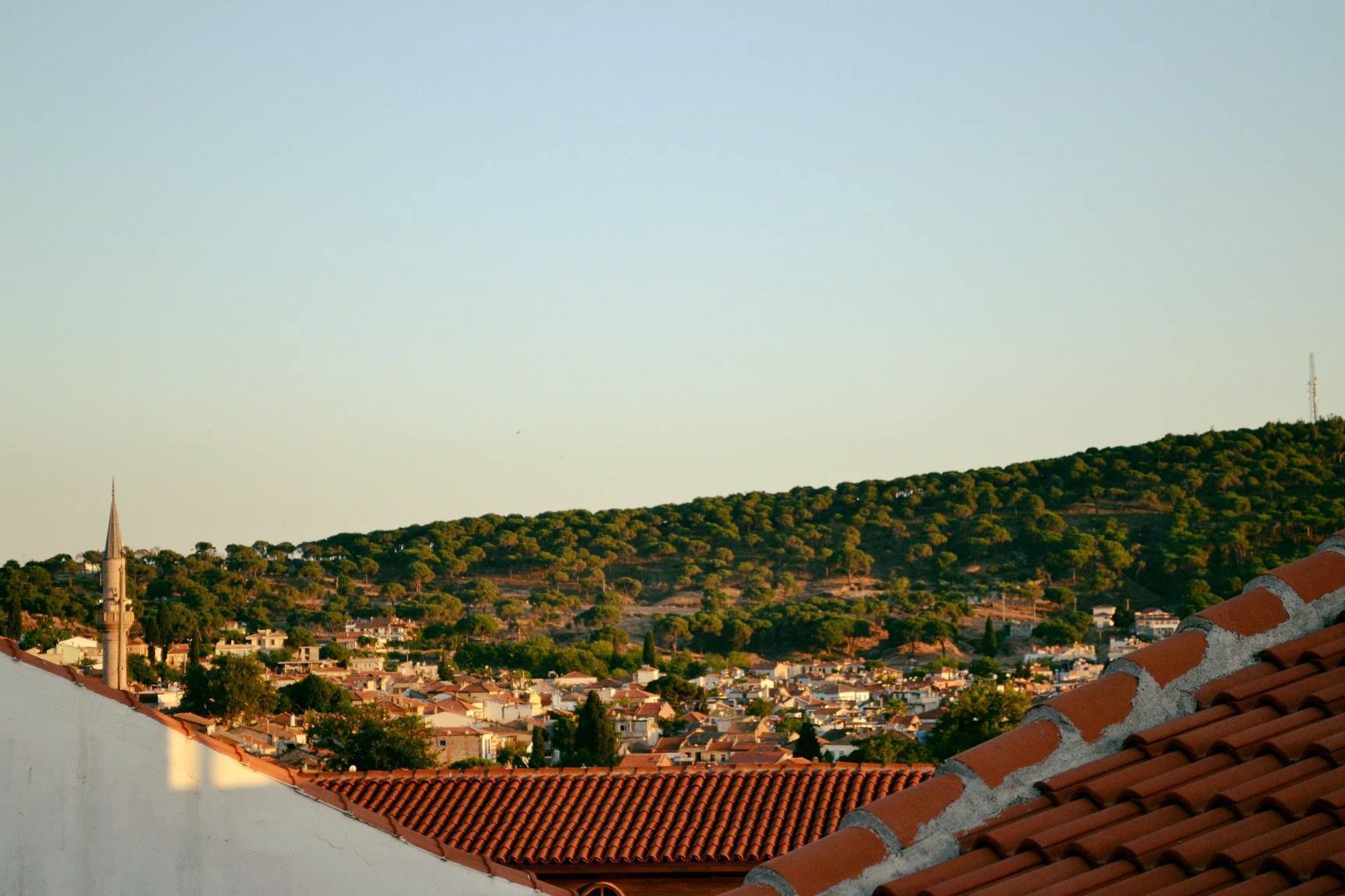 Eine Stadt mit einem markanten Kirchturm, Terrakotta-Dächern und einer hügeligen Landschaft im Hintergrund.