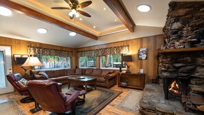 A cozy living room with a stone fireplace, leather chairs, a large sofa, and a wooden ceiling with exposed beams.