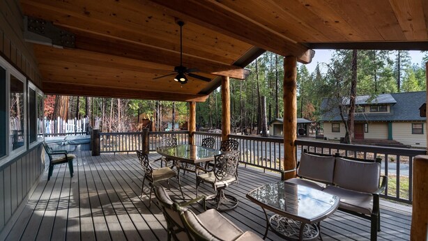 A wooden deck with outdoor seating, a ceiling fan, and a view of a forested area.