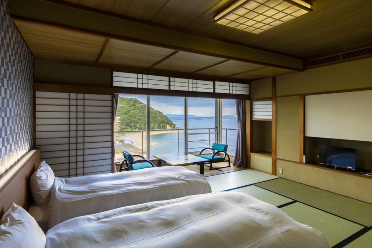 Ein traditioneller japanischer Raum mit Tatami-Böden, zwei Betten, einem Fernseher und Blick auf eine Küstenlandschaft.