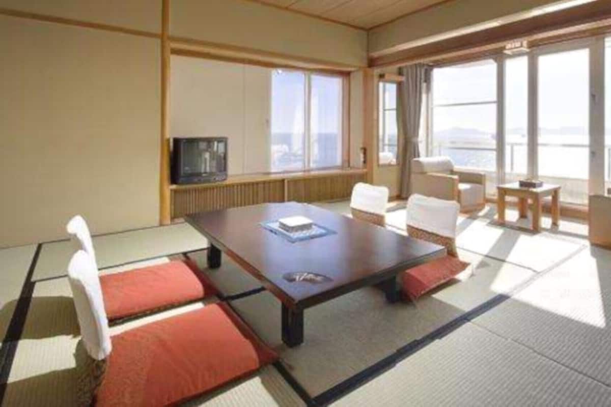 Ein Hotelzimmer mit großem Fenster, einem Fernseher, einem Esstisch und zwei Stühlen.
