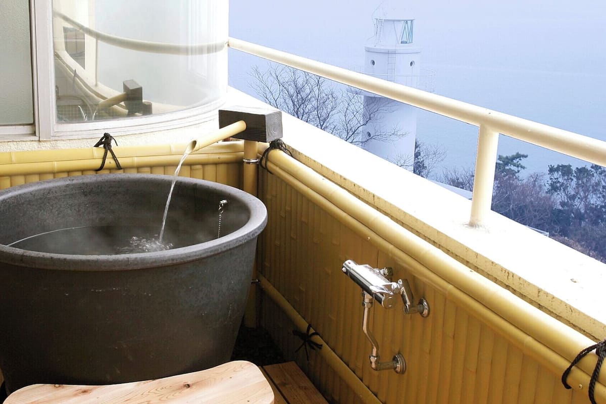 Ein Whirlpool mit einer Holzbank, einem Fenster und Blick auf einen Leuchtturm.