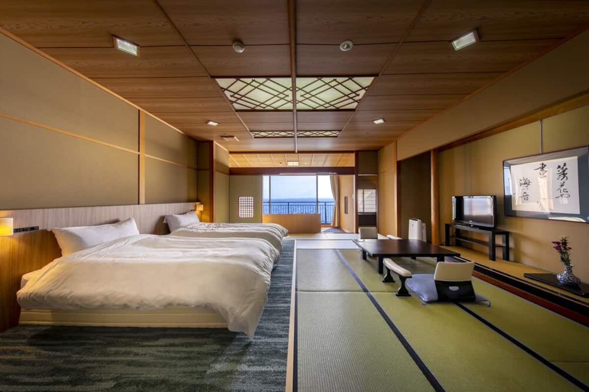 Ein traditionelles japanisches Hotelzimmer mit Tatami-Böden, einem großen Bett, einem Schreibtisch und einem Fernseher.