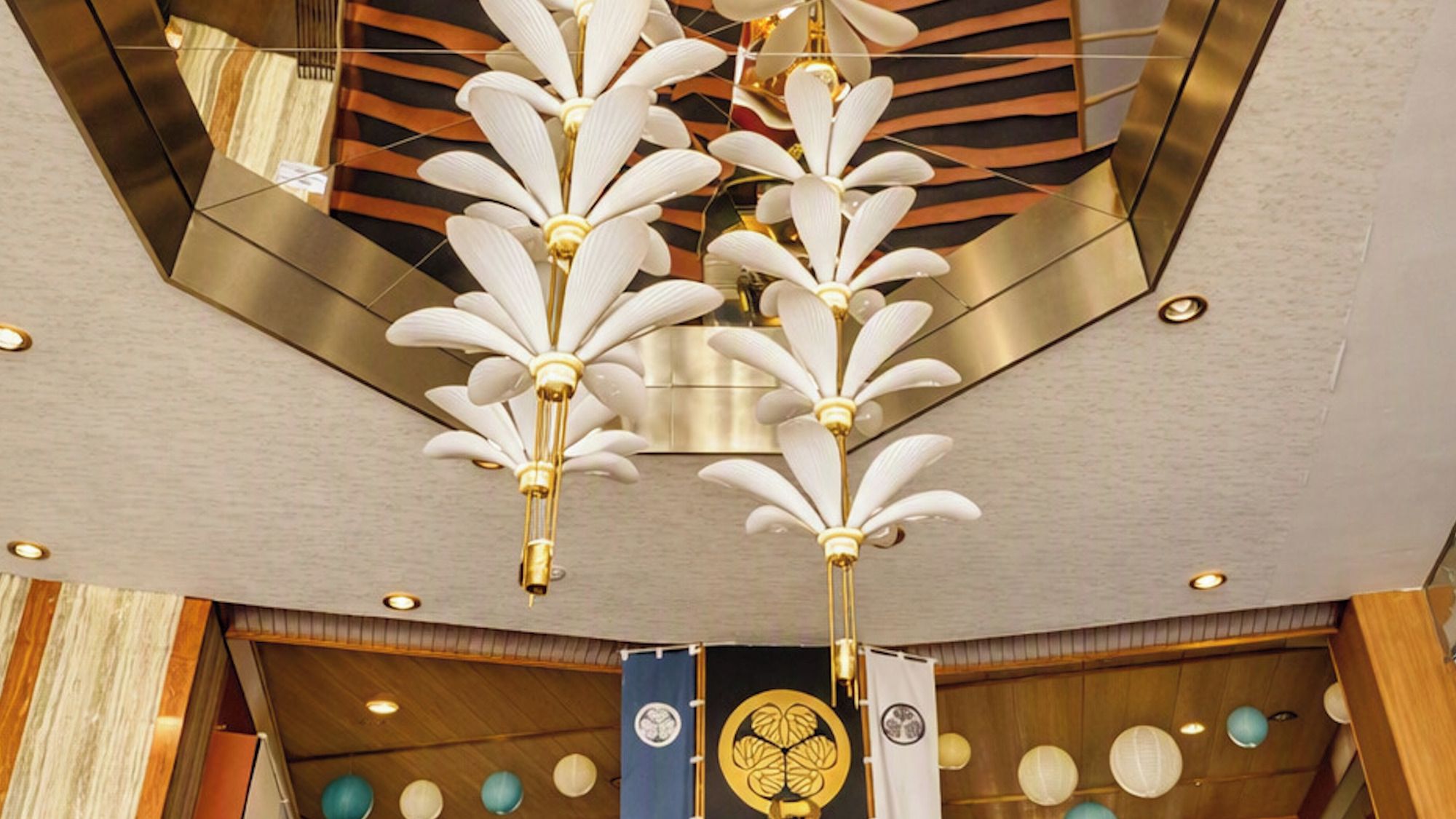 A ceiling with a geometric pattern and a central chandelier with white, leaf-like decorations.