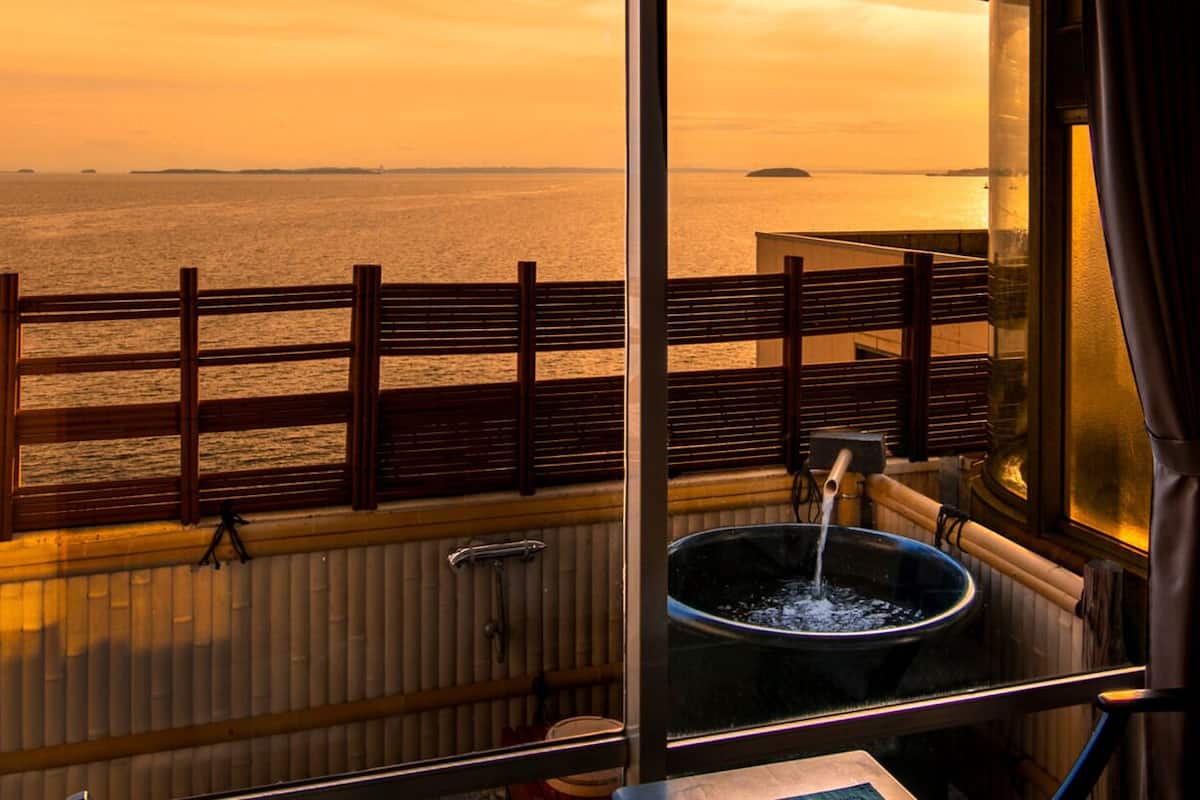 Ein Zimmer mit Meerblick bei Sonnenuntergang, ein Fenster mit Hollerkerung und ein Waschbecken mit fließendem Wasser.