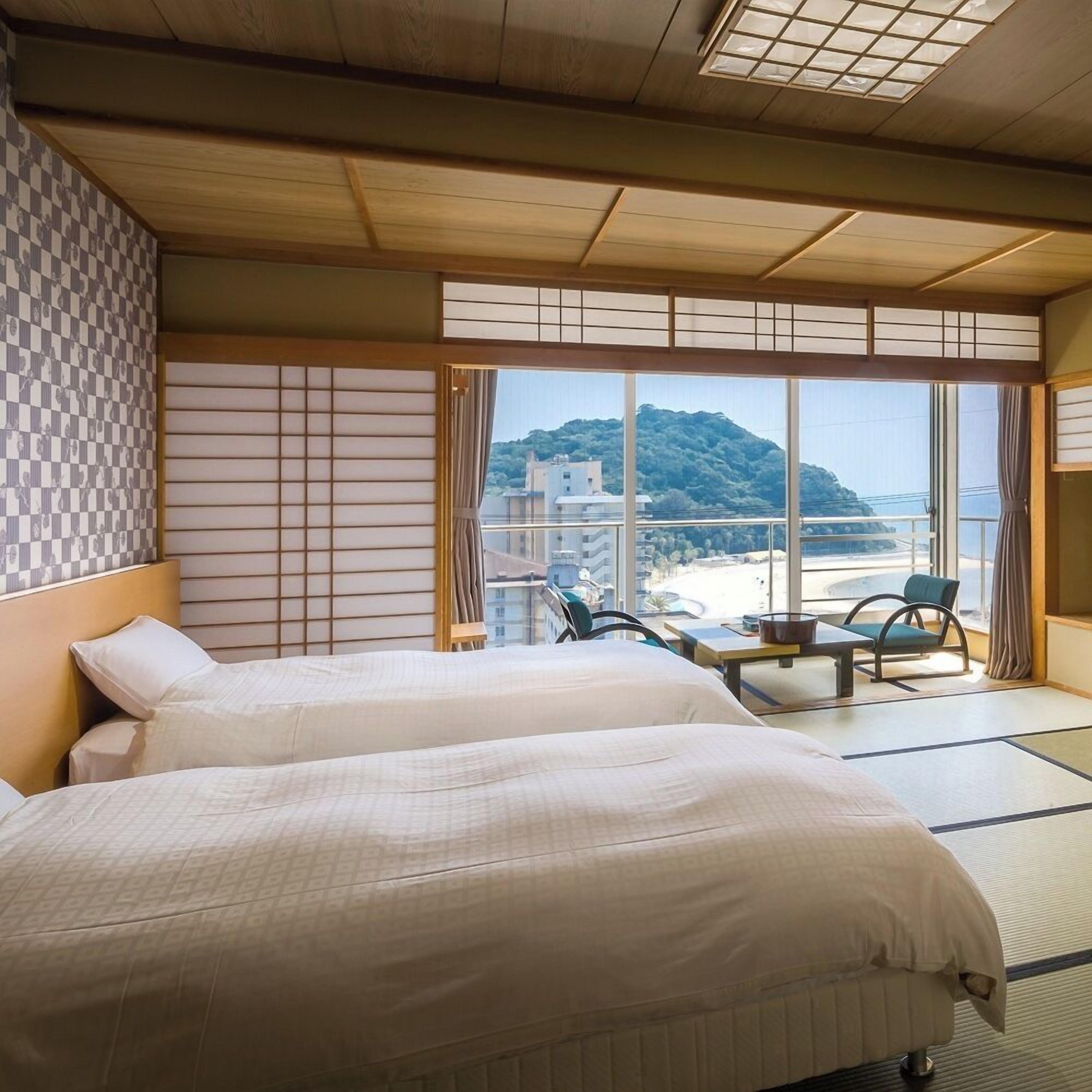 Une chambre d’hôtel avec deux lits, une vue sur la montagne et un balcon aménagé avec des sièges.