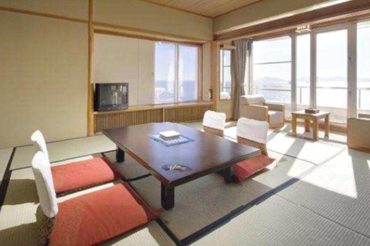 Una habitación de hotel con un ventanal grande, televisión, una mesa de comedor y dos sillas.