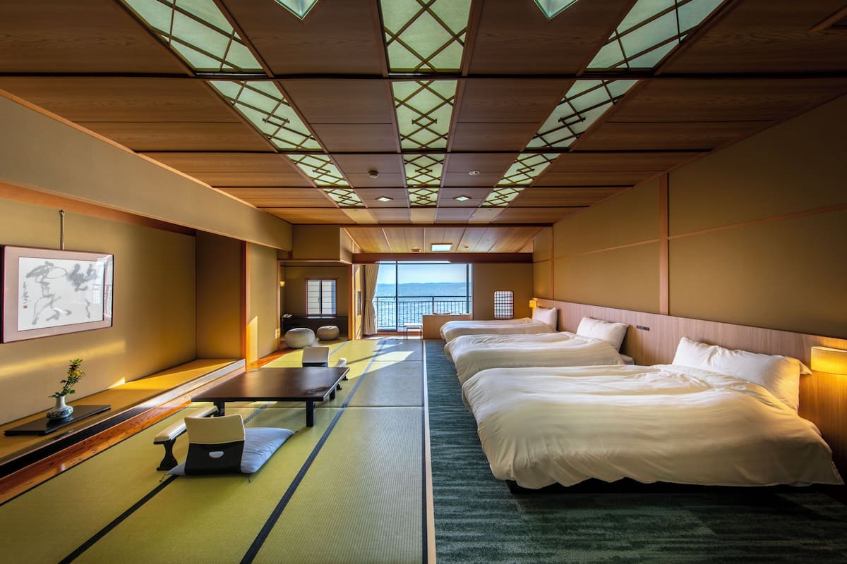 Ein Hotelzimmer mit Tatami-Boden, traditioneller japanischer Ästhetik, zwei Betten, einem Schreibtisch und Blick aufs Meer.