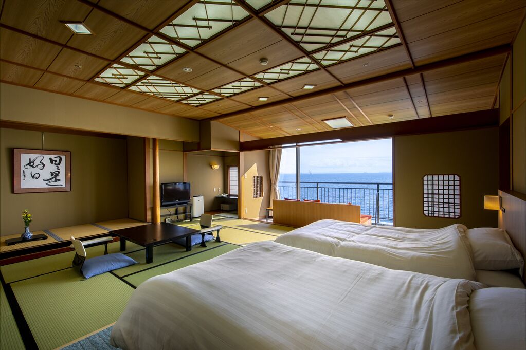 Une pièce de style japonais traditionnel, avec un sol recouvert de tatamis, un lit, une télévision et une vue sur la mer.