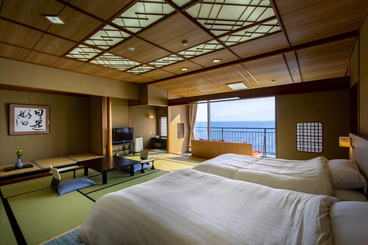 Ein traditioneller japanischer Raum mit Tatami-Böden, einem Bett, einem Fernseher und Meerblick.