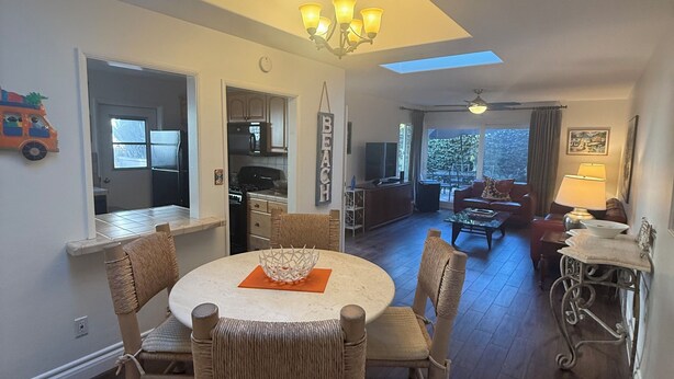 A dining area with a round table and wicker chairs, a chandelier, and a skylight above.