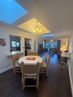 Relax in this open-plan living space featuring a dining area with a round table and wicker chairs, a kitchen, and a cozy seating area with a sofa and armchairs.