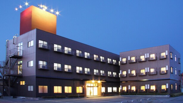 A multi-story hotel with a prominent red and brown facade, multiple balconies, and a well-lit entrance. - Hotel Isesaki East (Isesaki)