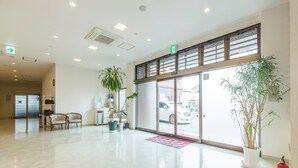 A spacious lobby with a polished floor, a reception desk, several chairs, and potted plants. - Hotel Isesaki East (Isesaki)