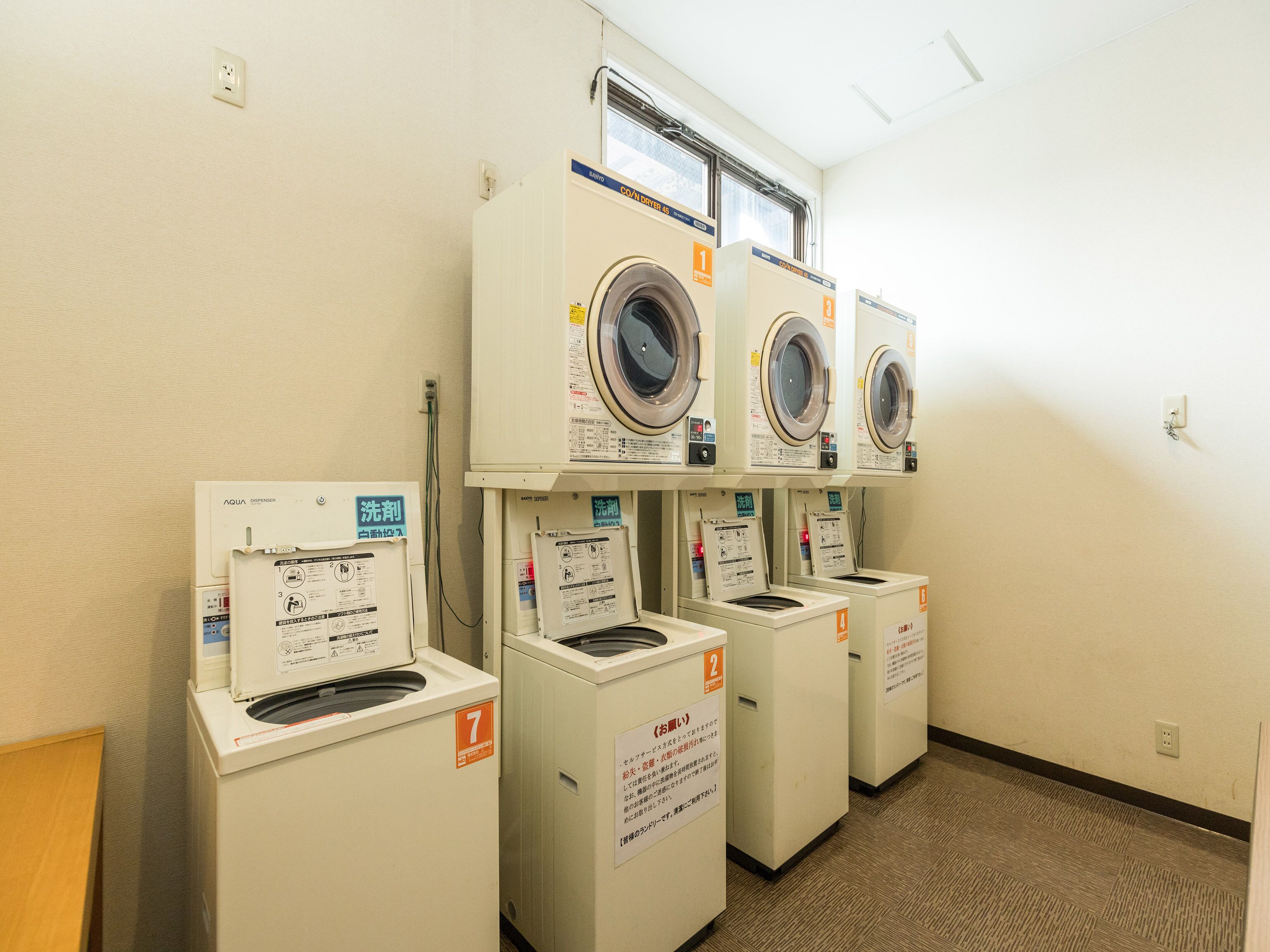 A laundry facility with seven washers and dryers, each marked with a number and instructions.